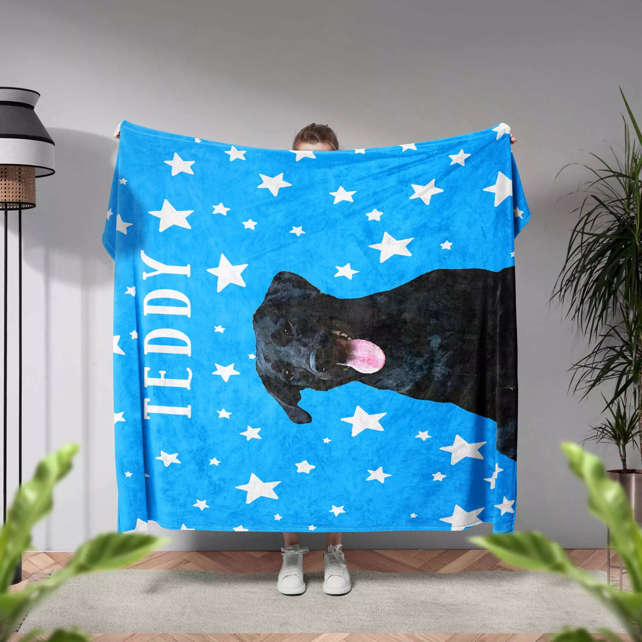 Person holding a blue dog blanket with a black dog and white stars, labeled 'TEDDY'.