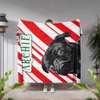 Person holding a Christmas blanket with a black Pug dog and 'Archie' text against a striped background