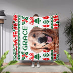 Person holding a Christmas ugly sweater custom made dog blanket with a dog's face and 'GRACE' text, surrounded by plants.