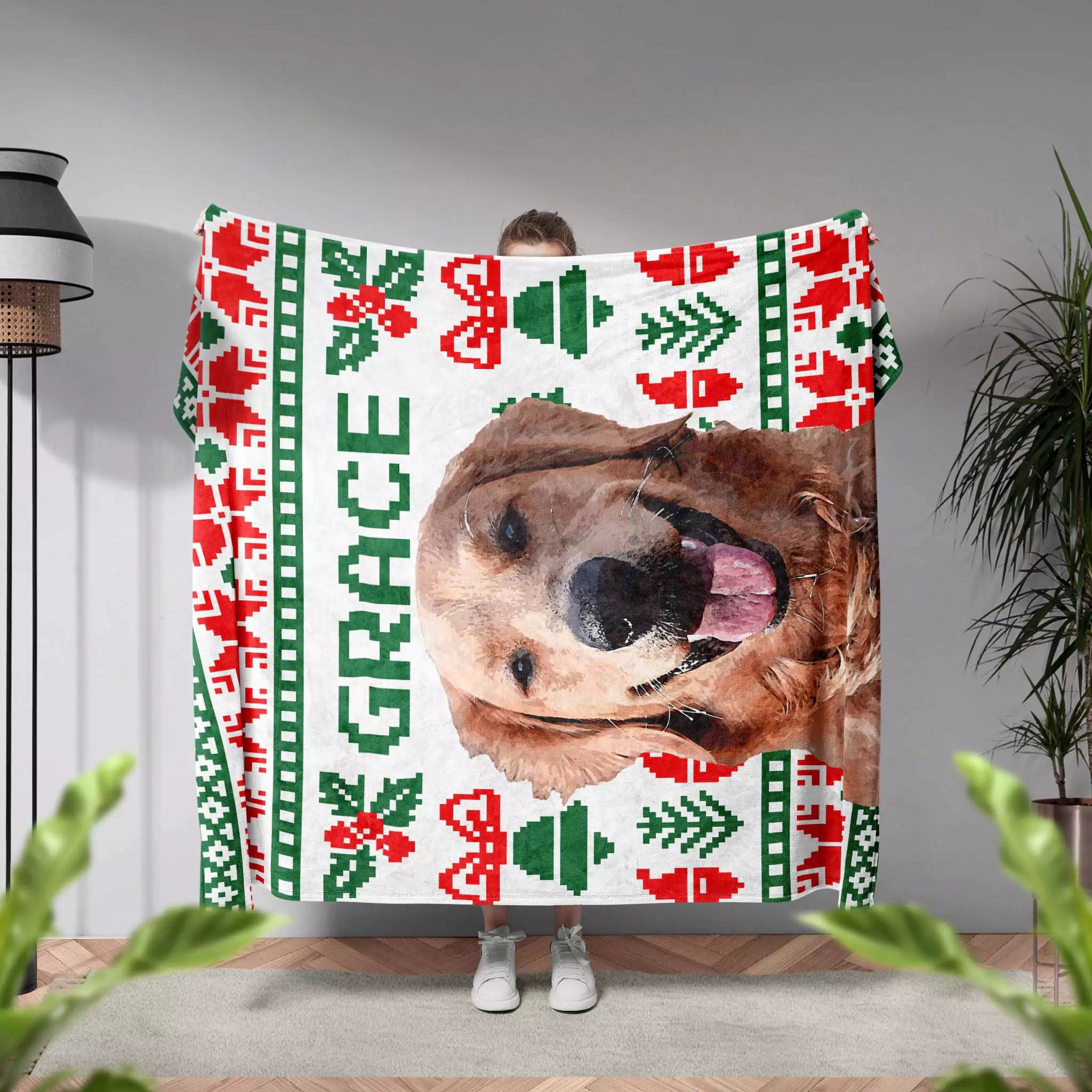 Person holding a Christmas ugly sweater custom made dog blanket with a dog's face and 'GRACE' text, surrounded by plants.