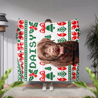 Person holding a dog blanket with a dog's face and 'Daisy' text, featuring Christmas patterns.