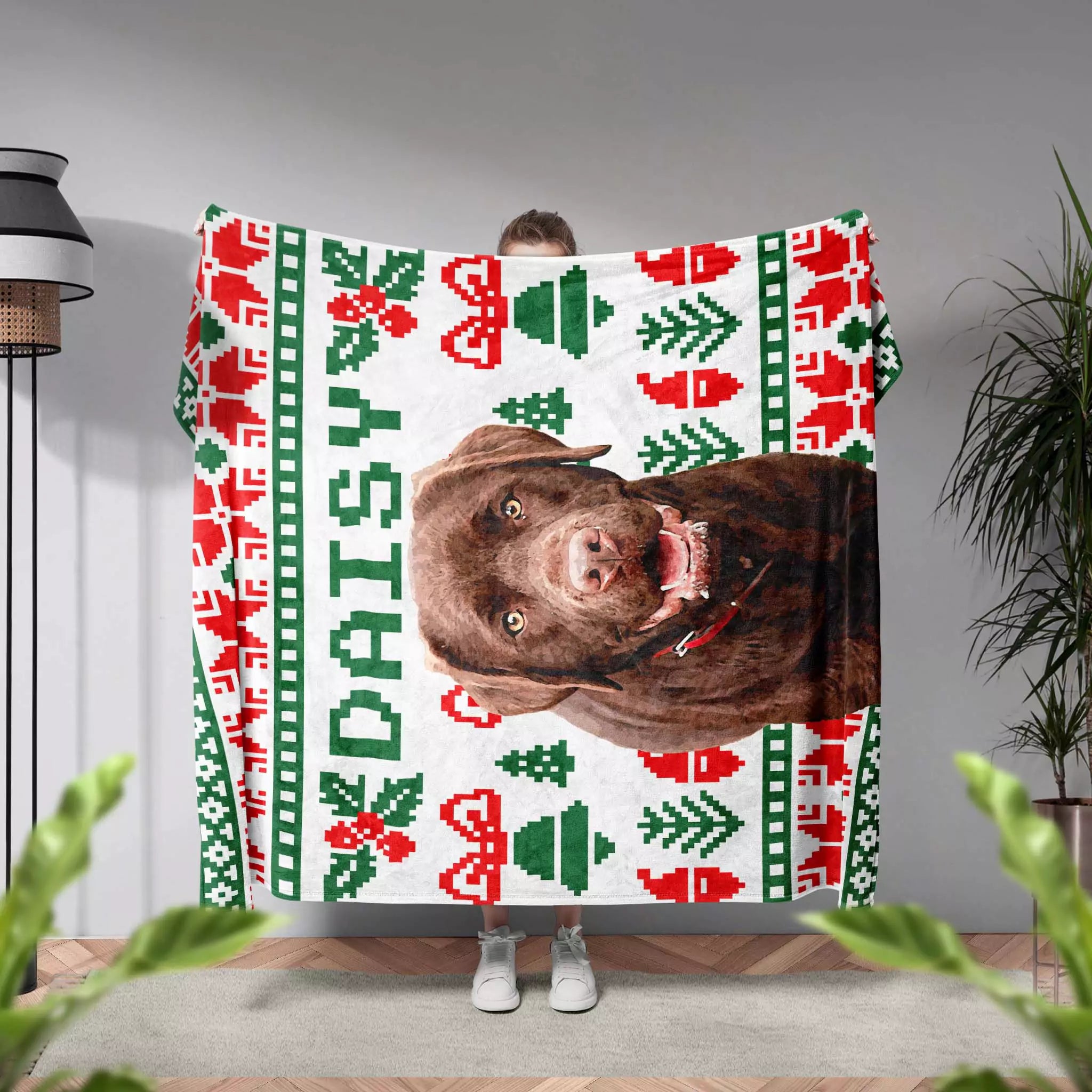 Person holding a dog blanket with a dog's face and 'Daisy' text, featuring Christmas patterns.