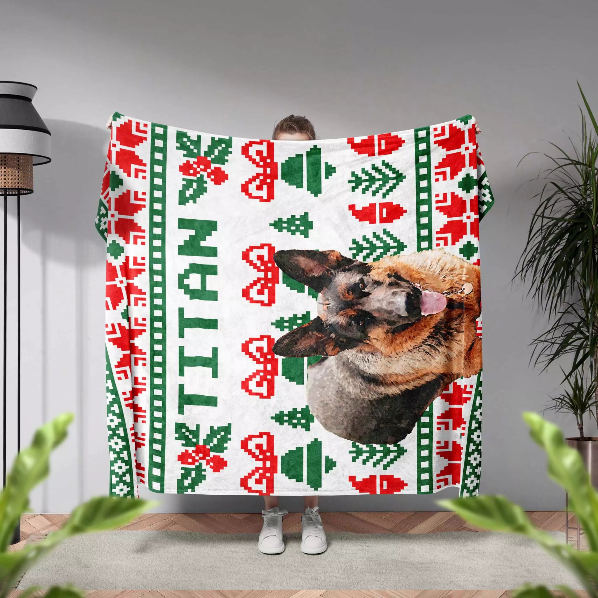Person holding a festive dog blanket with a dog's face printed on it, featuring red and green patterns.