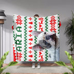Person holding a dog blanket with a dog design and dog name text in a room with plants and a lamp.