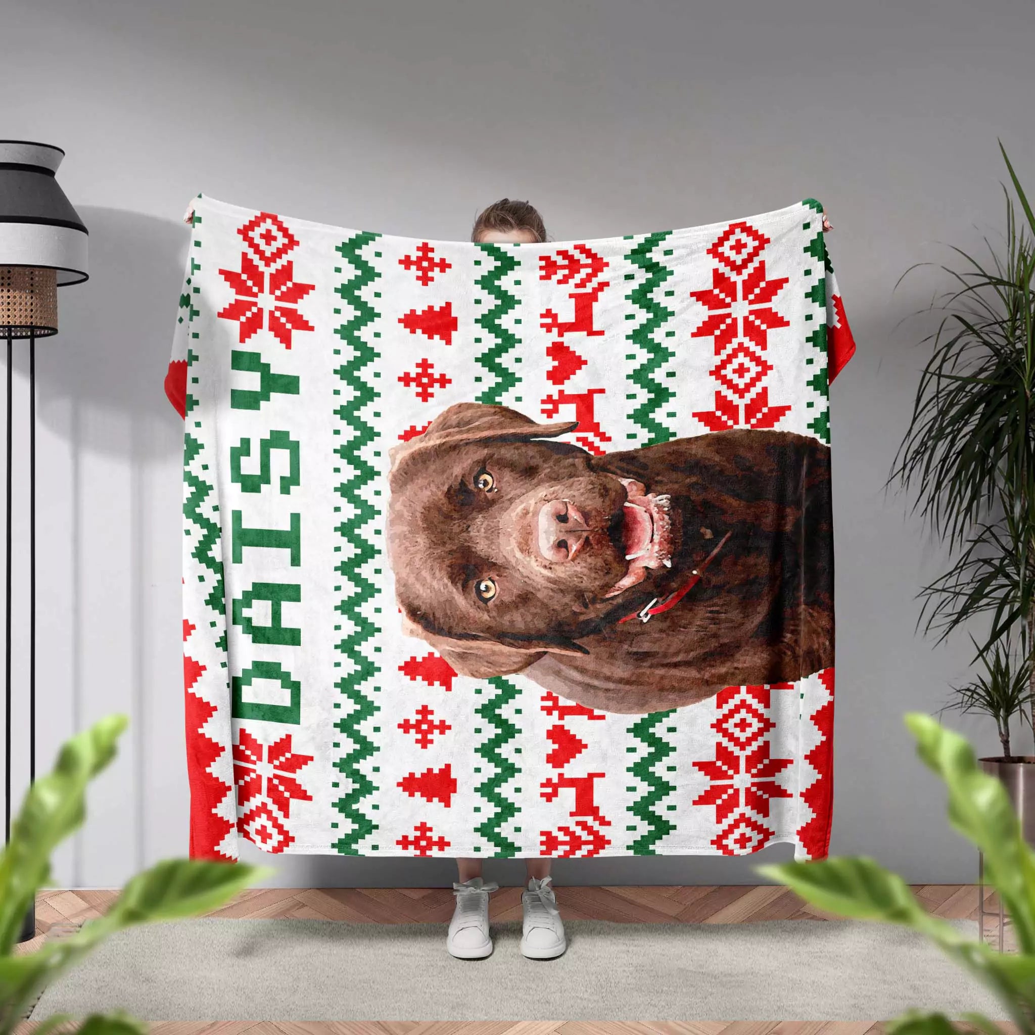 Person holding a dog blanket with a dog's face and 'Daisy' text against a neutral background