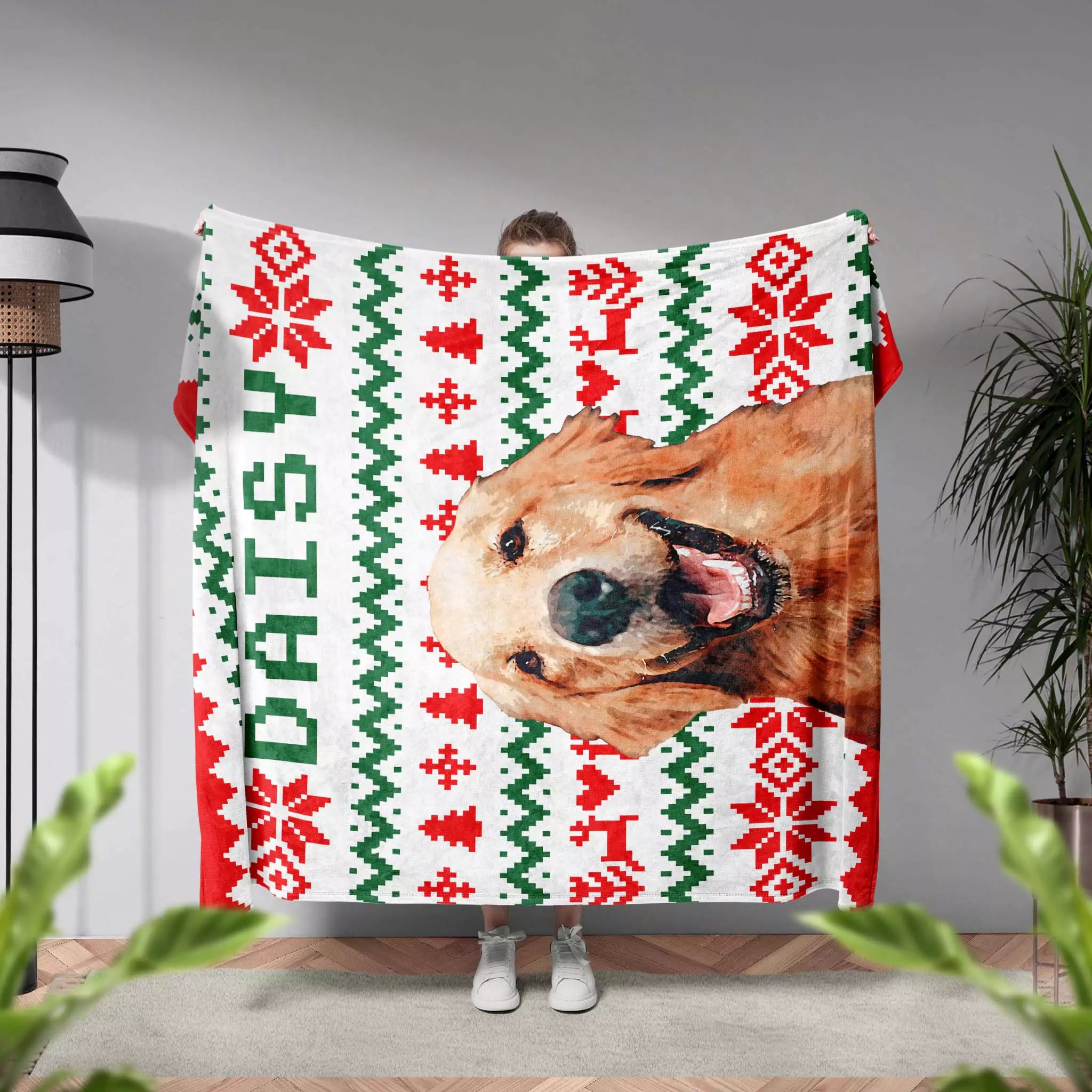 Person holding a blanket with a dog's face and ugly sweater Christmas pattern, with 'Daisy' written on it.