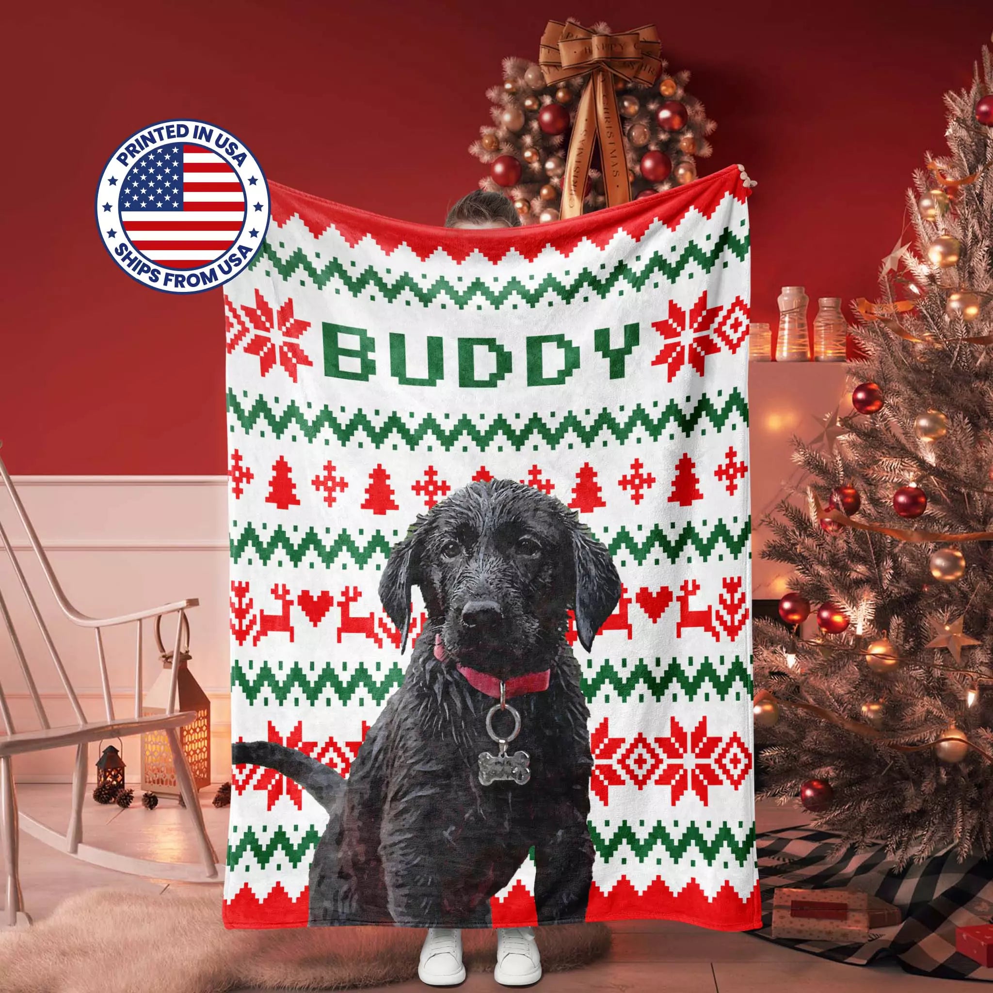 Retriever dog standing in front of an ugly sweater Christmas-themed blanket with 'Buddy' printed on it, in a festive room.